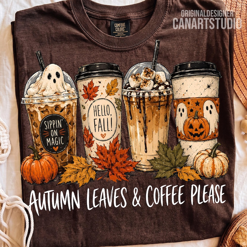 May include: A dark brown t-shirt featuring a graphic of four coffee cups decorated with autumn themes, including a ghost, a pumpkin, and the text 'Sippin' on Magic', 'Hello, Fall!', and 'Autumn Leaves & Coffee Please' printed in white lettering.