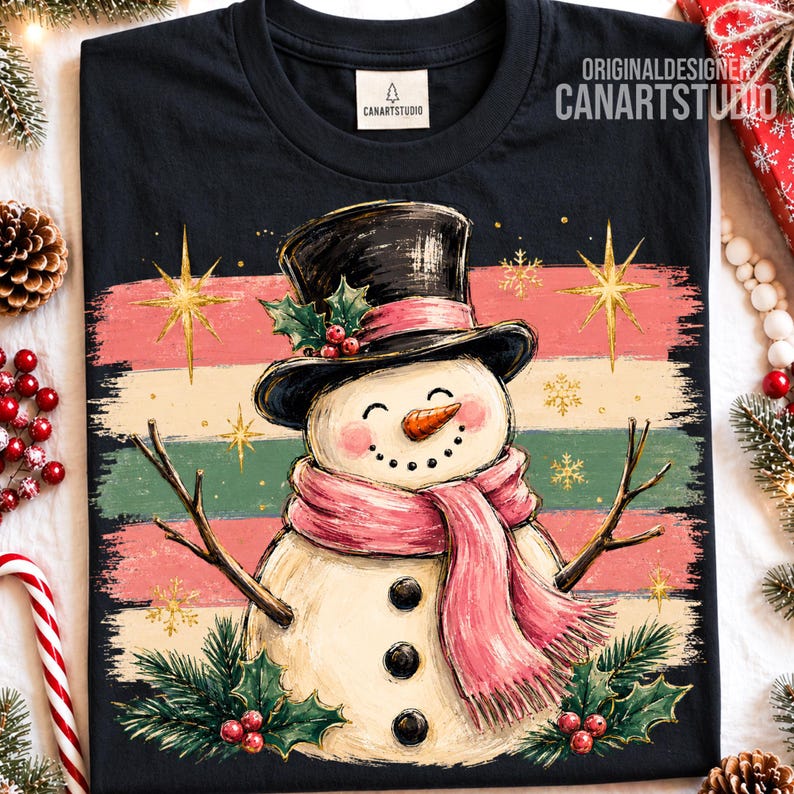 Może przedstawiać: Czarny t-shirt z grafiką uśmiechniętego bałwana w czarnym cylindrze i r&oacute;żowym szaliku. Wz&oacute;r zawiera poziome paski w kolorze r&oacute;żowym, kremowym i zielonym, złote gwiazdki, liście ostrokrzewu oraz jagody. Widoczny jest napis CANARTSTUDIO.