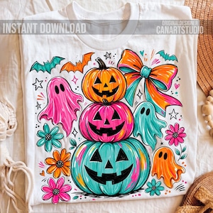 Op de afbeelding: Wit T-shirt met een kleurrijk Halloween-ontwerp. Het ontwerp toont gestapelde pompoenen, geesten, vleermuizen, bloemen en een grote strik. De tekst "INSTANT DOWNLOAD" is linksboven zichtbaar.