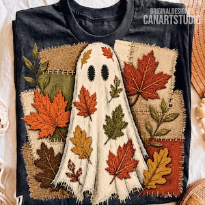 May include: A dark charcoal t-shirt featuring a graphic of a white ghost covered in autumn leaves. The design includes patches of burlap-textured fabric, red and orange maple leaves, and green foliage. The text ORIGINALDESIGN CANARTSTUDIO is visible.