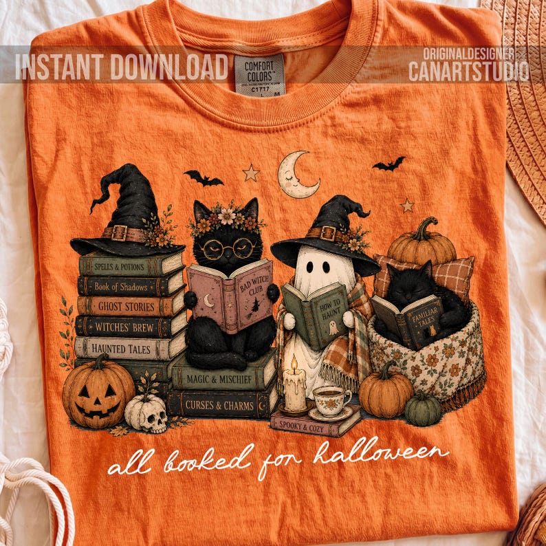 May include: An orange t-shirt featuring a graphic of two black cats and a ghost wearing witch hats, reading books stacked on top of each other. The design includes pumpkins, a skull, and the text "all booked for halloween" in white script.