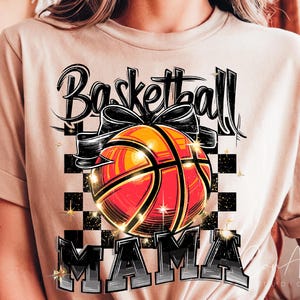 May include: A beige t-shirt featuring a graphic design of a basketball with a bow on top. The text "Basketball Mama" is printed below the basketball.