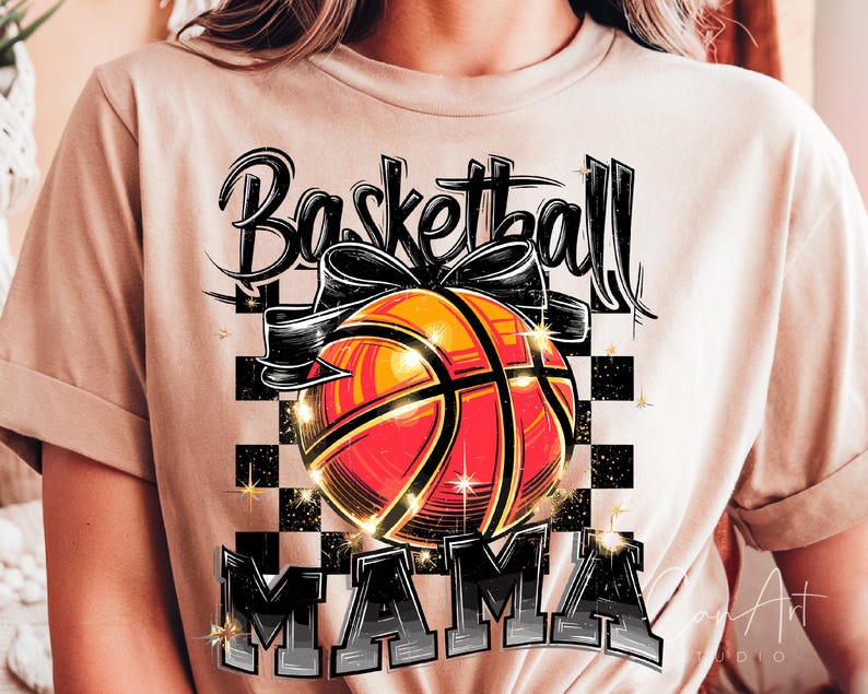 May include: A beige t-shirt featuring a graphic design of a basketball with a bow on top. The text "Basketball Mama" is printed below the basketball.