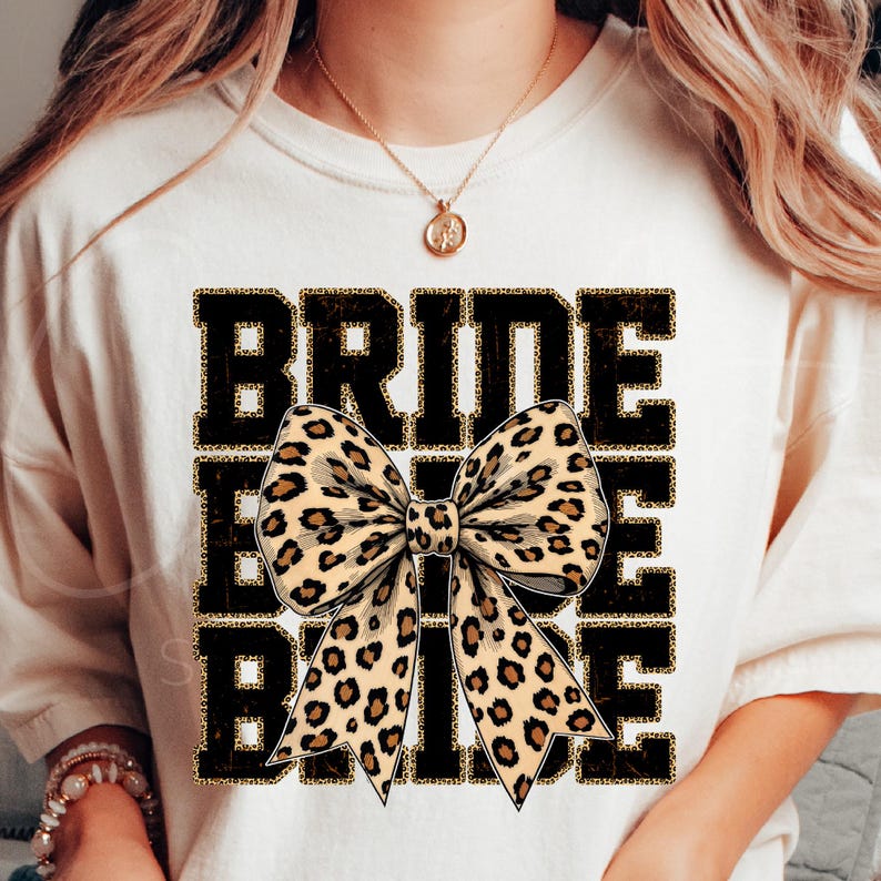 May include: White t-shirt with the text "BRIDE" in black with a gold glitter outline. A large leopard print bow is centred on the shirt.