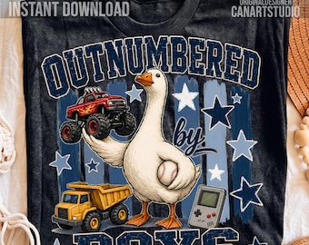 May include: A dark gray t-shirt featuring a white goose holding a baseball, surrounded by a red monster truck, a yellow dump truck, a handheld video game console, and blue stars. The text reads OUTNUMBERED by BOYS in a bold blue font.