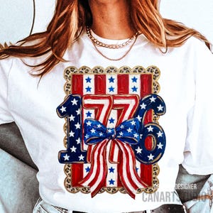 May include: White t-shirt with a patriotic design featuring the number "1776" in red, white, and blue. The design includes a bow and stars, set against a leopard print border. The shirt is a casual style.