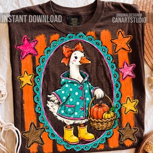 May include: A dark brown t-shirt featuring a graphic of a white goose wearing a teal polka-dot raincoat, a red bow, and yellow rain boots. The goose holds a basket of pumpkins inside a teal scalloped oval frame with orange stripes and stars.