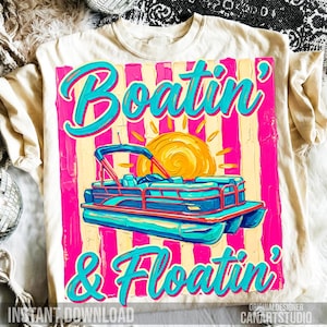 May include: Cream-colored t-shirt featuring a vibrant graphic with the words "Boatin' & Floatin'" in turquoise script. The design includes a turquoise and blue pontoon boat, a yellow sun, and pink and yellow vertical stripes.