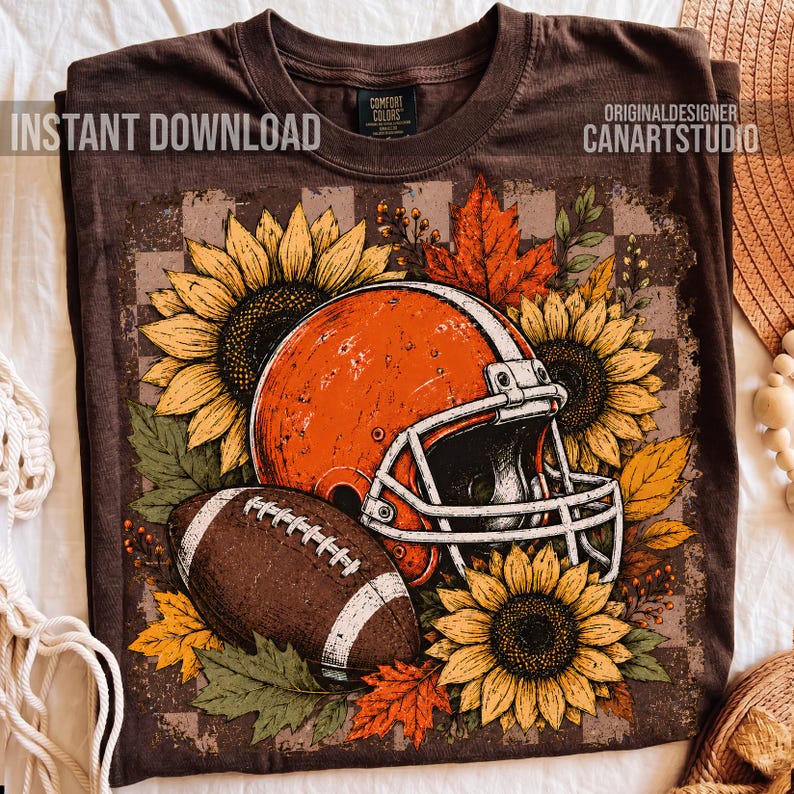 May include: A brown t-shirt featuring a graphic print of an orange football helmet, a brown football, yellow sunflowers, and orange autumn leaves. The text INSTANT DOWNLOAD and ORIGINALDESIGNER CANARTSTUDIO are printed on the shirt.