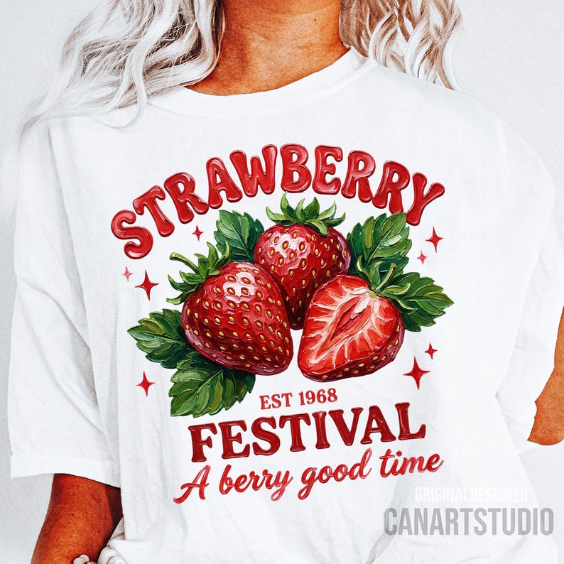 May include: White t-shirt with a strawberry-themed graphic. The design showcases three red strawberries, green leaves, and the words "STRAWBERRY FESTIVAL" with "EST 1968" and "A berry good time" in red text. The design is by CANARTSTUDIO.