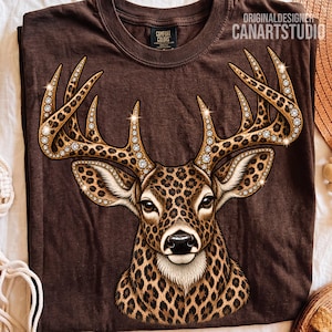 Könnte beinhalten: Ein dunkelbraunes T-Shirt mit einer Grafik eines Hirschkopfes mit Leopardenmuster und einem Geweih, das mit funkelnden, diamantartigen Akzenten verziert ist. Der Text ORIGINALDESIGNER CANARTSTUDIO steht in der oberen rechten Ecke.