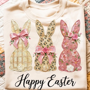 Puede incluir: Una sudadera de color crema con tres dise&ntilde;os decorativos de conejos. Cada conejo tiene un patr&oacute;n &uacute;nico y est&aacute; adornado con lazos y detalles florales. Las palabras "Happy Easter" est&aacute;n escritas en cursiva debajo de los conejos.