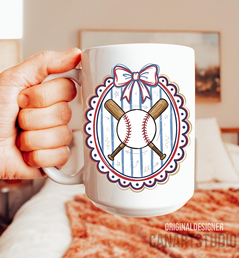 May include: White ceramic mug featuring a baseball design. The design includes a baseball, crossed bats, and a bow, all within a decorative oval frame. The mug has the text "ORIGINAL DESIGNER CANARTSTUDIO" at the bottom.