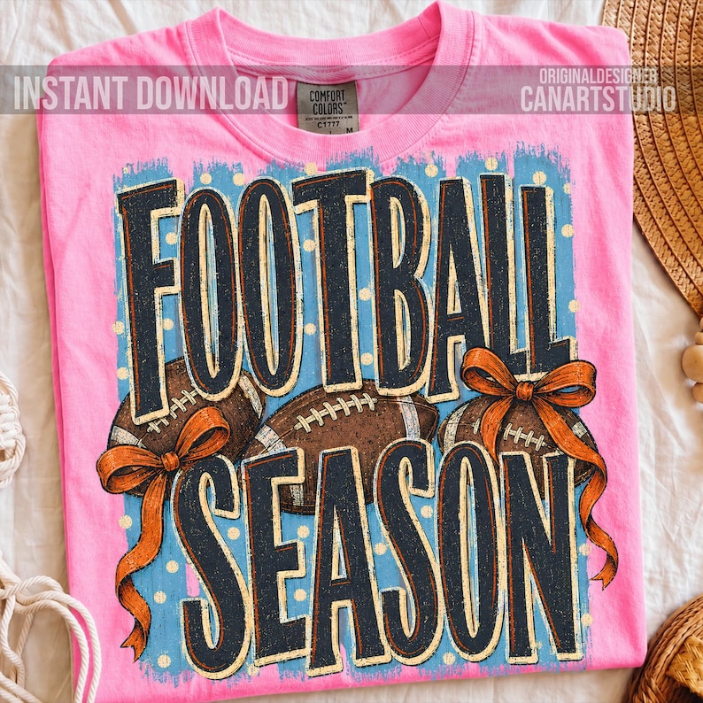 K&ouml;nnte beinhalten: Ein leuchtend pinkes T-Shirt mit dem Schriftzug FOOTBALL SEASON in gro&szlig;en dunkelblauen Buchstaben. Das Design zeigt zwei braune Footballs und zwei orangefarbene Schleifen auf hellblauem Grund mit wei&szlig;en Punkten. Das Shirt hat ein Comfort Colors Etikett.