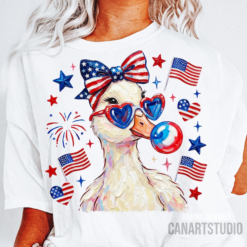 Op de afbeelding: Wit T-shirt met een grillige eend met een hartvormige zonnebril en een patriottische strik. De eend blaast een bel, omringd door Amerikaanse vlaggen en sterren. De tekst "CANARTSTUDIO" staat onderaan.