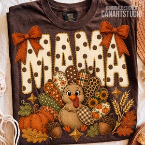May include: A dark brown t-shirt featuring the word MAMA in large cream letters with brown polka dots. Two orange bows are attached to the top of the letters. A turkey graphic with patterned feathers, a pumpkin, acorns, and wheat stalks are below.