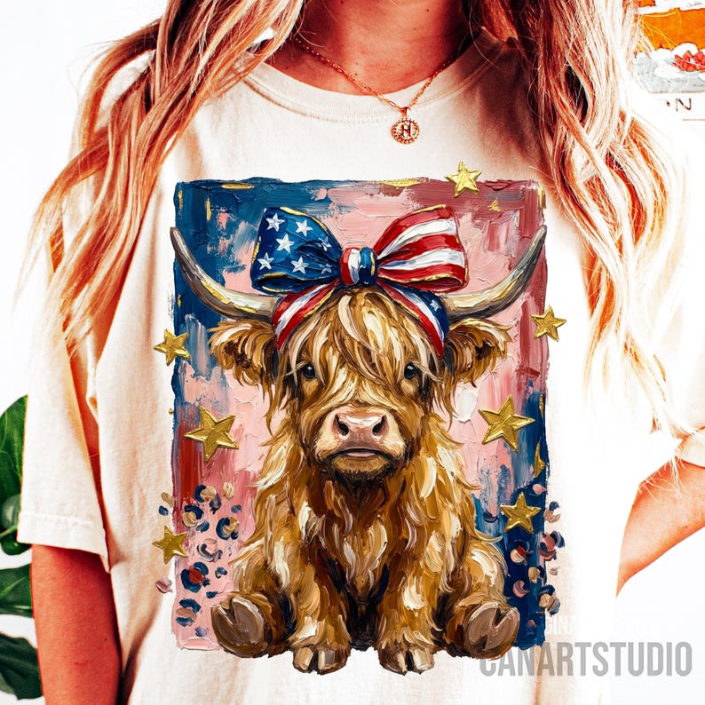 Peut inclure: T-shirt cr&egrave;me avec une peinture color&eacute;e d'une vache des Highlands orn&eacute;e d'un n&oelig;ud et d'un bandeau aux couleurs du drapeau am&eacute;ricain. Le fond pr&eacute;sente des accents bleus, roses et dor&eacute;s, avec des &eacute;toiles dor&eacute;es et des d&eacute;tails l&eacute;opard. Le texte "CANARTSTUDIO" est visible.