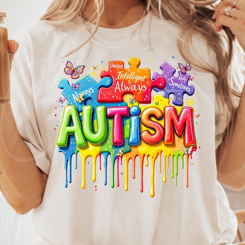 May include: A white t-shirt with a colorful graphic design of puzzle pieces that spell out "AUTISM". The puzzle pieces have words on them, including "Unique", "Intelligent", "Always", "Totally", and "Sometimes".