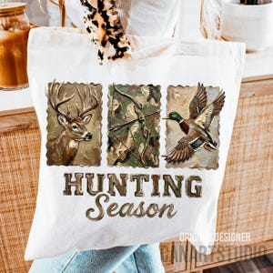 May include: A white tote bag featuring three rectangular images: a deer, a bow and arrow, and a duck in flight. The words "HUNTING Season" are printed in a brown, textured font below the images. The bag has a hunting theme.