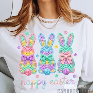 May include: White t-shirt featuring three colorful crochet Easter bunnies with bows and star accents. The words "happy easter" are embroidered in pastel colors. The design includes the text "ORIGINAL DESIGNER CANARTS STUDIO".