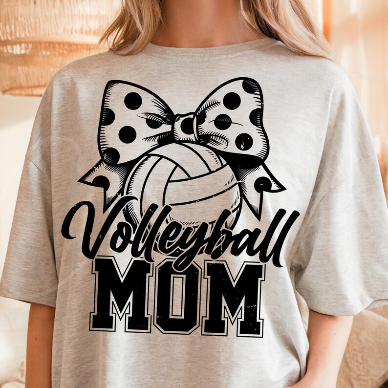 May include: A gray t-shirt with a black and white volleyball and bow with polka dots. The text "Volleyball Mom" is printed in black.