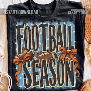 K&ouml;nnte beinhalten: Ein schwarzes T-Shirt mit einer Grafik, die den Schriftzug "FOOTBALL SEASON" in gro&szlig;en, dunklen Buchstaben zeigt. Das Design umfasst zwei braune Footballs, einen hellblauen Hintergrund mit wei&szlig;en Punkten und eine orangefarbene Schleife.