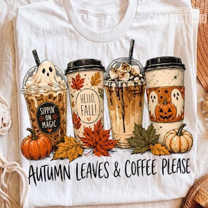 May include: A white t-shirt featuring a graphic of four coffee cups decorated with autumn themes, including a ghost, pumpkins, and fall leaves. The text reads Sippin' on Magic, Hello, Fall!, and Autumn Leaves & Coffee Please in black lettering.
