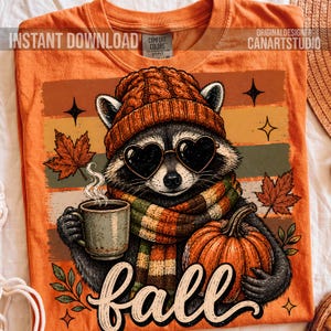 Puede incluir: Una camiseta naranja con el gr&aacute;fico de un mapache que lleva un gorro de punto y una bufanda a rayas, sosteniendo una taza humeante y una calabaza. El mapache lleva gafas de sol en forma de coraz&oacute;n. El dise&ntilde;o incluye hojas y la palabra fall.