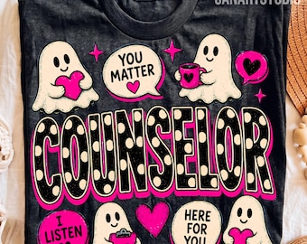 May include: A black t-shirt featuring a graphic print of four white ghosts, pink hearts, and speech bubbles with the text YOU MATTER, I LISTEN, and HERE FOR YOU. The word COUNSELOR is printed in large black letters with white polka dots.
