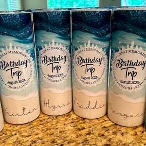 May include: Four personalized tumblers with a beach scene and the text "Birthday Trip - August 2023". The tumblers are labeled with the names "Kristen", "Alyssa", "Maddie", and "Margaret".