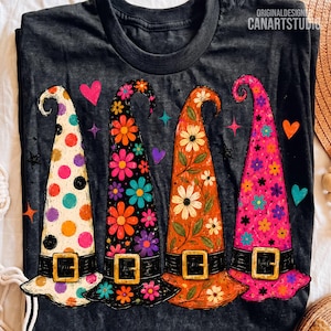Op de afbeelding: Een antracietgrijs t-shirt met vier hoge, puntige hoeden met zwarte banden en gouden gespen. De hoeden hebben kleurrijke patronen, waaronder stippen, levendige bloemenprints en kleine sterren, geaccentueerd door verspreide hartvormen.