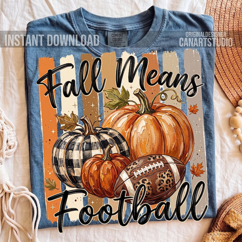 May include: Blue t-shirt with a fall-themed graphic. The design features pumpkins, a football with a leopard print, and the text "Fall Means Football." Vertical stripes in orange, brown, and beige are behind the pumpkins.