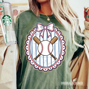 May include: Green baseball-themed t-shirt with a baseball and crossed bats design. The design includes a red, white, and blue color scheme with a bow at the top. The text "CANARTSTUDIO" is visible at the bottom.