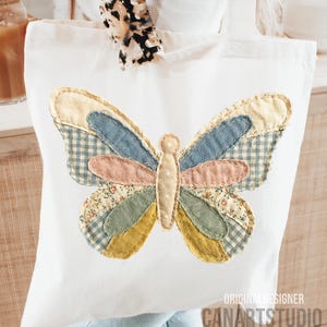 May include: White tote bag featuring a colorful butterfly applique. The butterfly design incorporates various fabrics in shades of blue, pink, yellow, and green. The text "ORIGINAL DESIGNER CANARTSTUDIO" is printed on the bottom right corner.