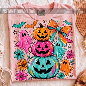 Op de afbeelding: Roze T-shirt met een kleurrijk Halloween-ontwerp. Het ontwerp toont gestapelde pompoenen, geesten, vleermuizen, bloemen en een grote strik. De tekst "INSTANT DOWNLOAD" en "ORIGINAL DESIGNER CANARTSTUDIO" staat op het shirt.