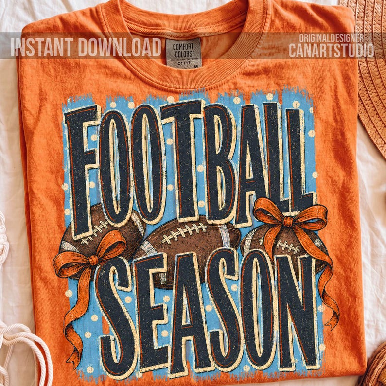 K&ouml;nnte beinhalten: Ein orangefarbenes T-Shirt mit kurzen &Auml;rmeln und einem Grafikdruck mit dem Text FOOTBALL SEASON in dunkelblauen Buchstaben. Das Design zeigt zwei braune Footballs und zwei orangefarbene Schleifen auf hellblauem Grund mit wei&szlig;en Punkten.