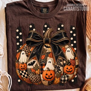Peut inclure: Un t-shirt marron foncé avec un grand motif de citrouille orné d'un nœud noir. La citrouille présente des motifs léopard, à carreaux et des feuilles d'automne, avec des illustrations de fantômes et de chauves-souris. Texte : ORIGINALDESIGNER CANARTSTUDIO.