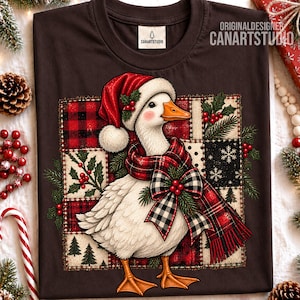 Può includere: Una t-shirt marrone scuro con la grafica di un'oca bianca che indossa un cappello da Babbo Natale rosso e una sciarpa a quadri rossi e neri con un fiocco abbinato. L'oca è posizionata davanti a uno sfondo patchwork quadrato con agrifoglio.