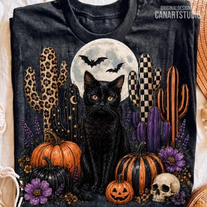 May include: A black t-shirt featuring a graphic of a black cat sitting before a full moon with two bats, surrounded by patterned cacti, orange and black pumpkins, a jack-o'-lantern, purple flowers, and a skull. The text CANARTSTUDIO is visible.