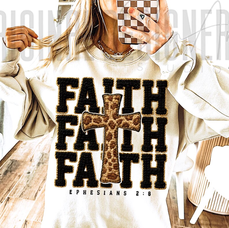 May include: Cream-colored sweatshirt with the word "FAITH" in black block letters, repeated three times. A cross with a leopard print design is centered within the word "FAITH". The text "EPHESIANS 2:8" is printed below the word "FAITH".