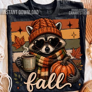 Puede incluir: Una camiseta negra con el gr&aacute;fico de un mapache que lleva un gorro de punto naranja, gafas de sol en forma de coraz&oacute;n y una bufanda a rayas. El mapache sostiene una taza humeante y una calabaza. El fondo tiene hojas de oto&ntilde;o y el texto "fall".