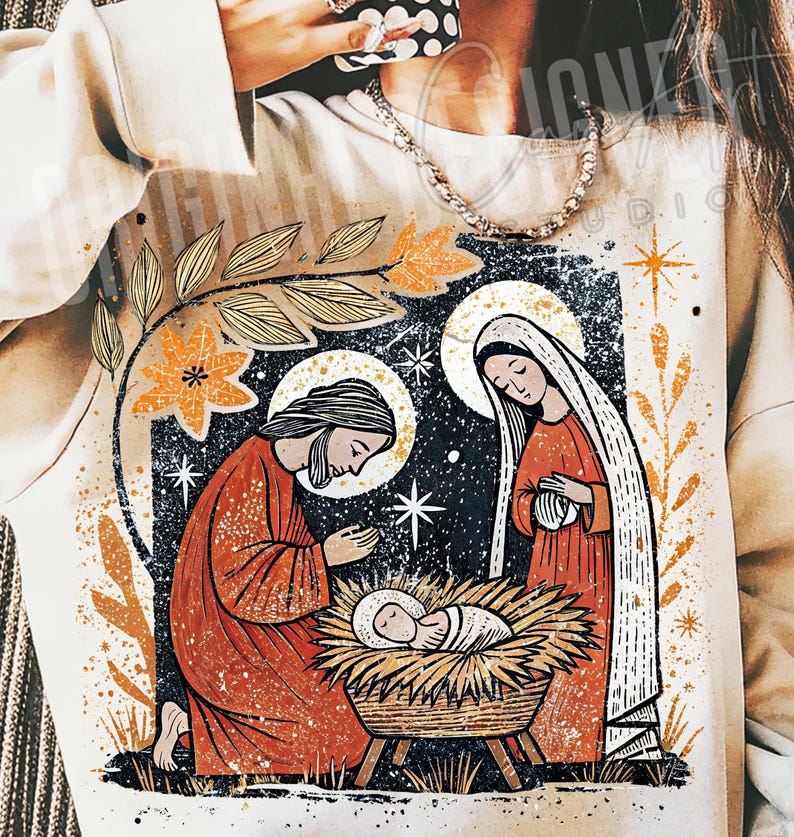 May include: A cream-colored sweatshirt featuring a graphic illustration of the Nativity scene. The design includes Joseph, Mary, and baby Jesus in a manger, with a starry night background and floral accents in orange and gold.