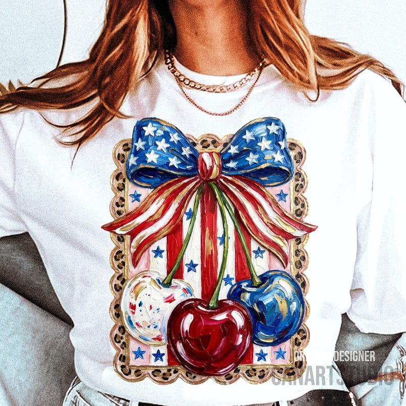 May include: White t-shirt featuring a patriotic design with a bow and cherries. The bow is blue with white stars, and the cherries are red, white, and blue. The design is framed with a leopard print border.