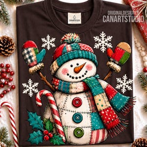 May include: A dark brown t-shirt featuring a graphic of a snowman with a patchwork-style hat, scarf, and mittens. The snowman has an orange carrot nose, a black dotted smile, and three colorful buttons. White snowflakes and holly leaves surround the figure.