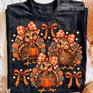 Puede incluir: Una camiseta gris carbón oscuro con un gráfico de tres pavos marrones con lazos de cuadros naranjas y blancos, detalles de estampado de leopardo y calabazas naranjas. El diseño incluye lazos naranjas y lunares blancos sobre un fondo oscuro.