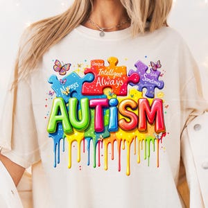 May include: A white t-shirt with a colorful graphic design of puzzle pieces and the word "AUTISM". The puzzle pieces have text on them that reads "Unique", "Intelligent & Always", "Totally Sometimes Mysterious".