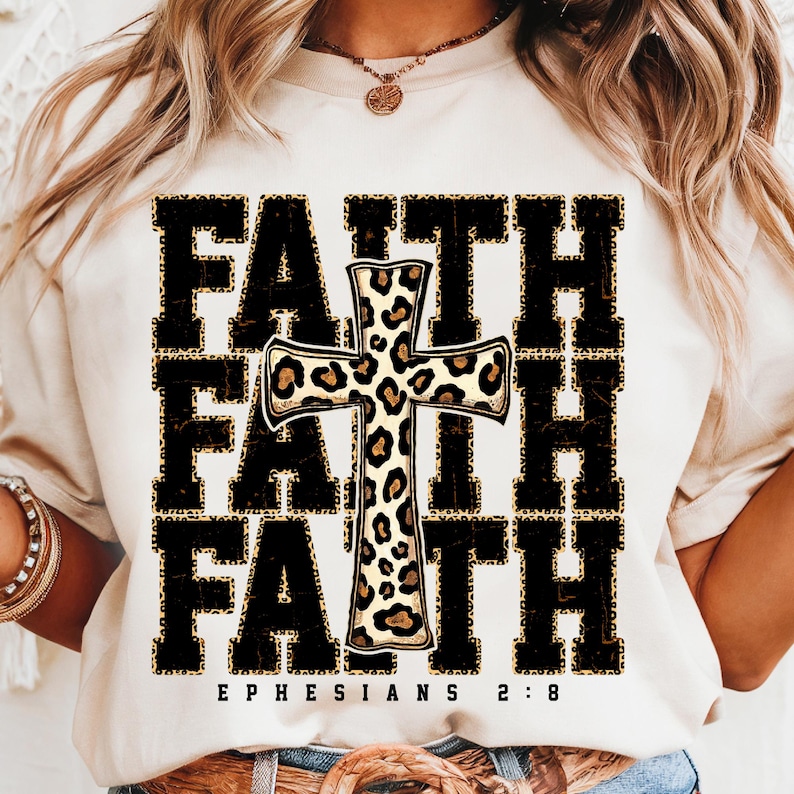 May include: White t-shirt with a black and gold graphic of the word "FAITH" repeated three times with a leopard print cross in the center. The text "EPHESIANS 2:8" is printed below the graphic.