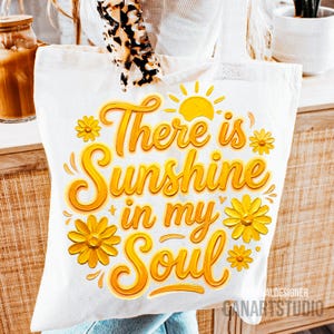 Peut inclure: Sac fourre-tout blanc avec l'inscription "There is Sunshine in my Soul" en lettres jaunes. Le motif comprend des fleurs jaunes et un soleil. Le sac est en tissu clair.