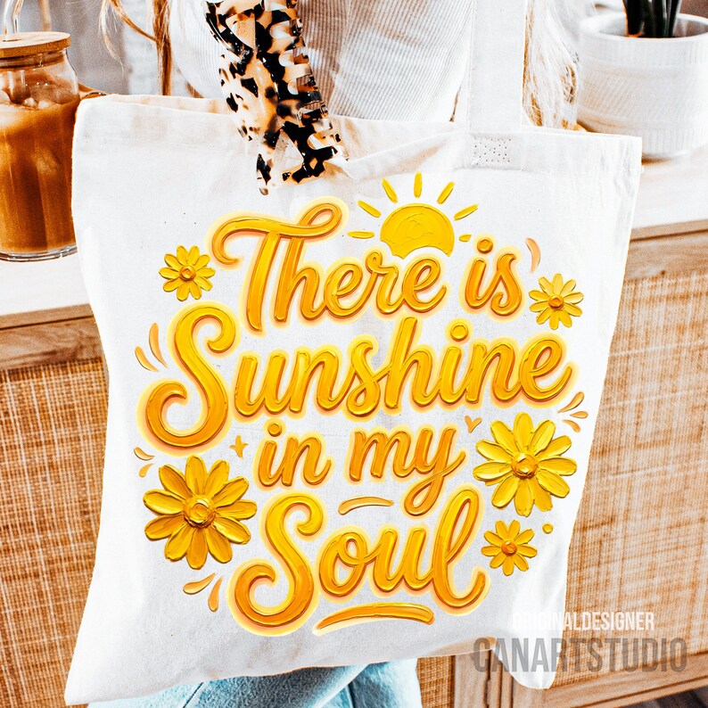 Peut inclure: Sac fourre-tout blanc avec l'inscription "There is Sunshine in my Soul" en lettres jaunes. Le motif comprend des fleurs jaunes et un soleil. Le sac est en tissu clair.