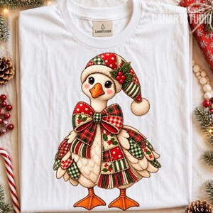 Könnte beinhalten: Ein weißes T-Shirt mit einer Grafik einer Gans, die eine weihnachtliche Patchwork-Mütze und eine große passende Patchwork-Schleife trägt. Die Gans hat orangefarbene Füße und einen Schnabel, mit rot-grün-weißem Karomuster und Punkten.